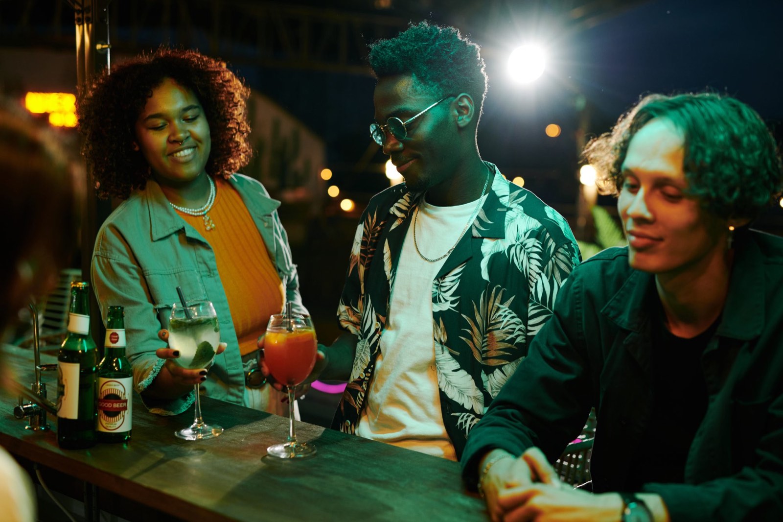Três amigos num bar à noite, com drinks na mesa.